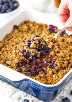 blueberry crisp in casserole dish with a scoop being taken out