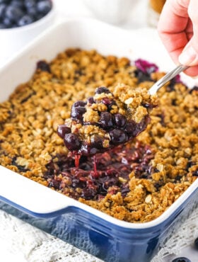 blueberry crisp in casserole dish with a scoop being taken out