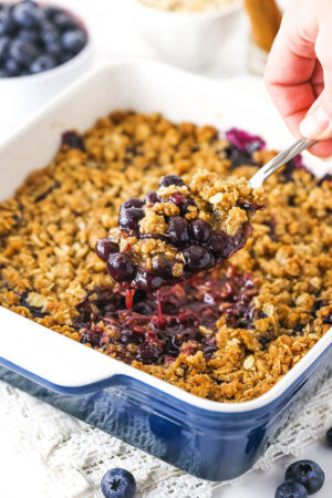 blueberry crisp in casserole dish with a scoop being taken out