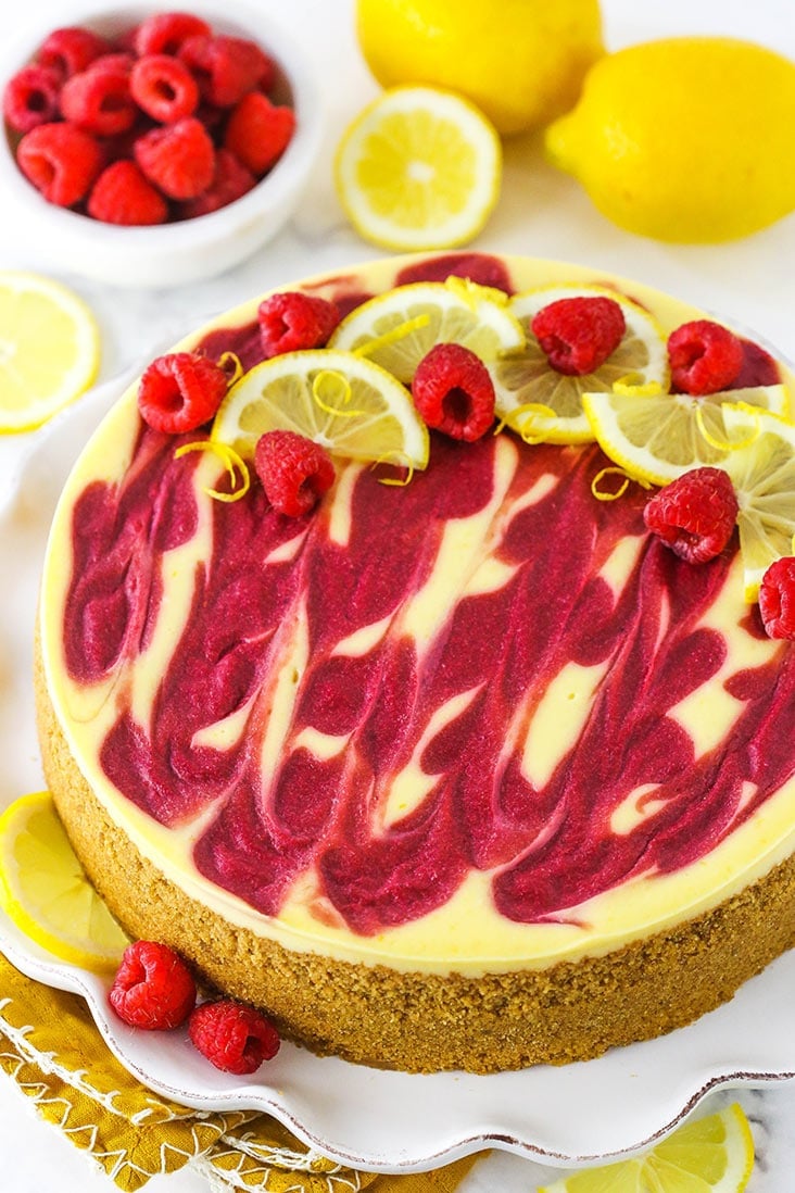 A lemon raspberry swirl cheesecake topped with fresh raspberries and lemon slices