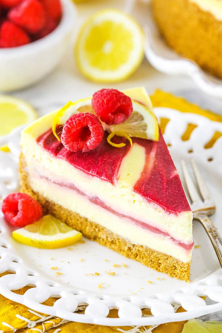 A slice of lemon cheesecake with raspberry swirl, topped with raspberries and lemon
