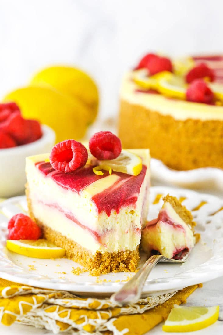 A slice of lemon raspberry swirl cheesecake topped with raspberries and lemon