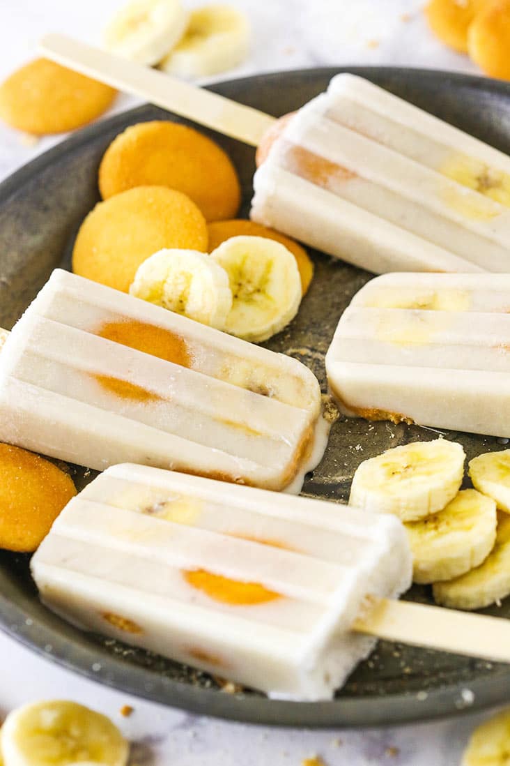 A King of Pops copycat recipe, these Banana Pudding Popsicles are creamy, indulgent & refreshing. All your favorite banana pudding flavors! Banana popsicles on a tray with vanilla wafers and banana slices