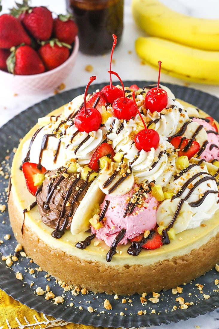 banana split cheesecake on dark grey serving tray with fruit in the background