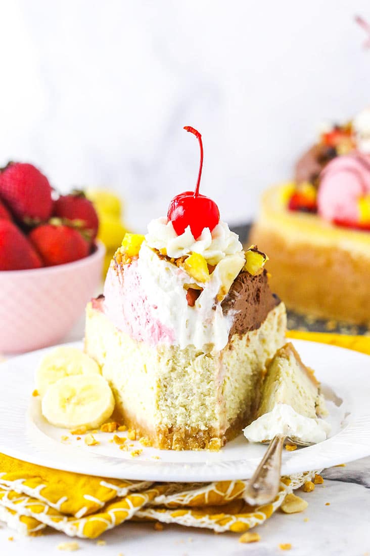 slice of banana split cheesecake on white plate with bite taken