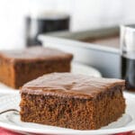 slice of coca cola cake on white plate with glass of coke in background