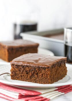 slice of coca cola cake on white plate with glass of coke in background