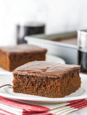 slice of coca cola cake on white plate with glass of coke in background