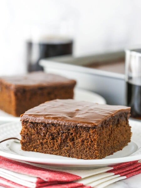slice of coca cola cake on white plate with glass of coke in background