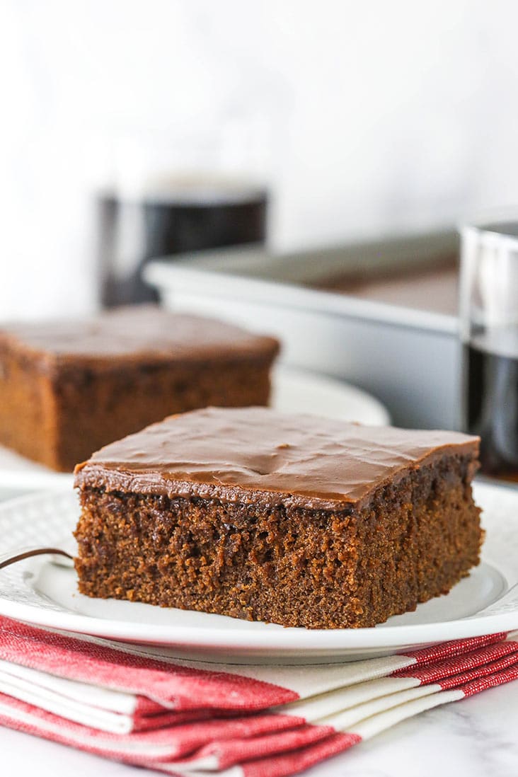 slice of coca cola cake on white plate with glass of coke in background