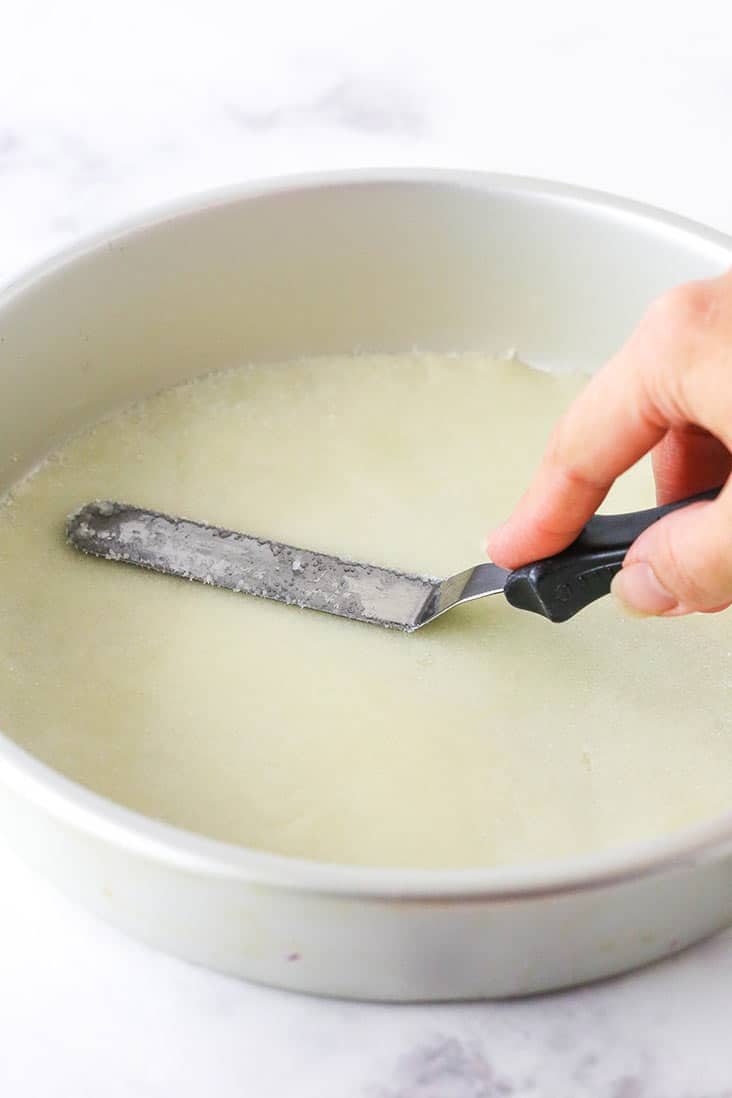 A spatula spreading a butter and sugar mixture on the bottom of a pan