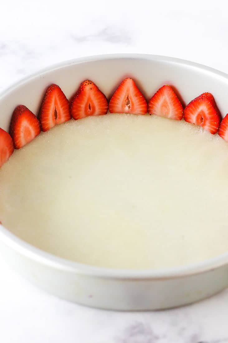 A round pan with a layer of sugar and butter and sliced strawberries around the edges