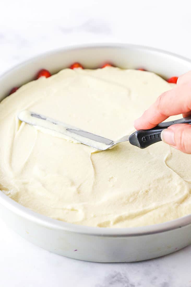 Cake batter being spread over sliced strawberries in a cake pan