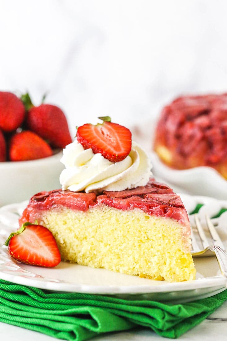 A slice of strawberry upside down cake topped with whipped cream and a fresh strawberry