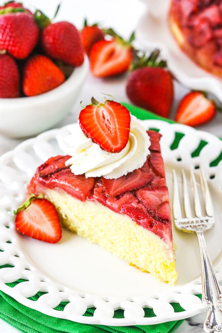 A slice of strawberry upside down cake topped with whipped cream and a fresh strawberry