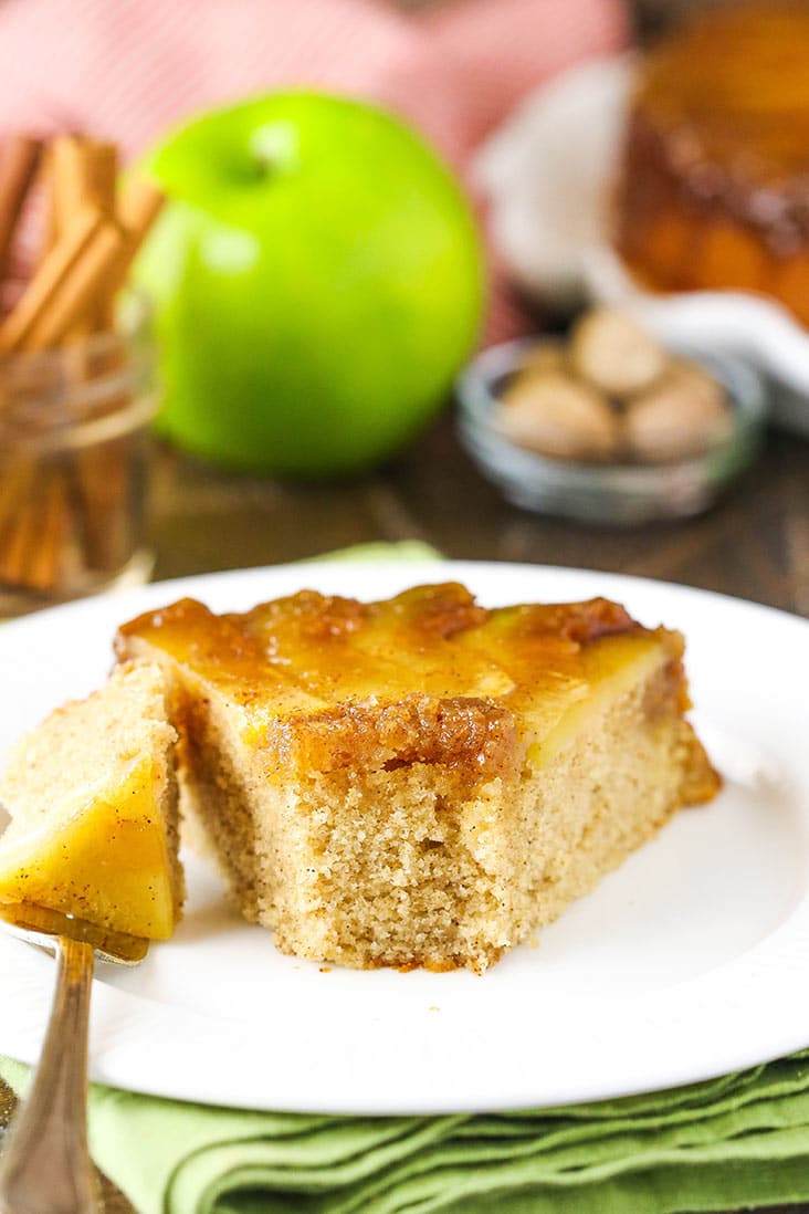 A slice of apple upside down cake on a white plate with a bite missing