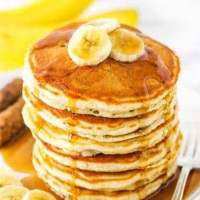 Banana pancakes stacked high on a plate with syrup and banana slices