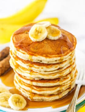 Banana pancakes stacked high on a plate with syrup and banana slices