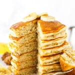 A stack of banana pancakes with one piece missing and slices of bananas on top