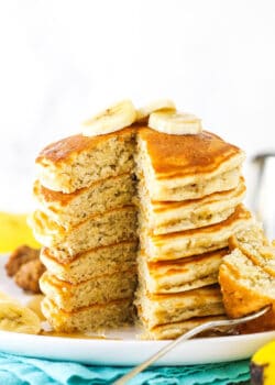 A stack of banana pancakes with one piece missing and slices of bananas on top