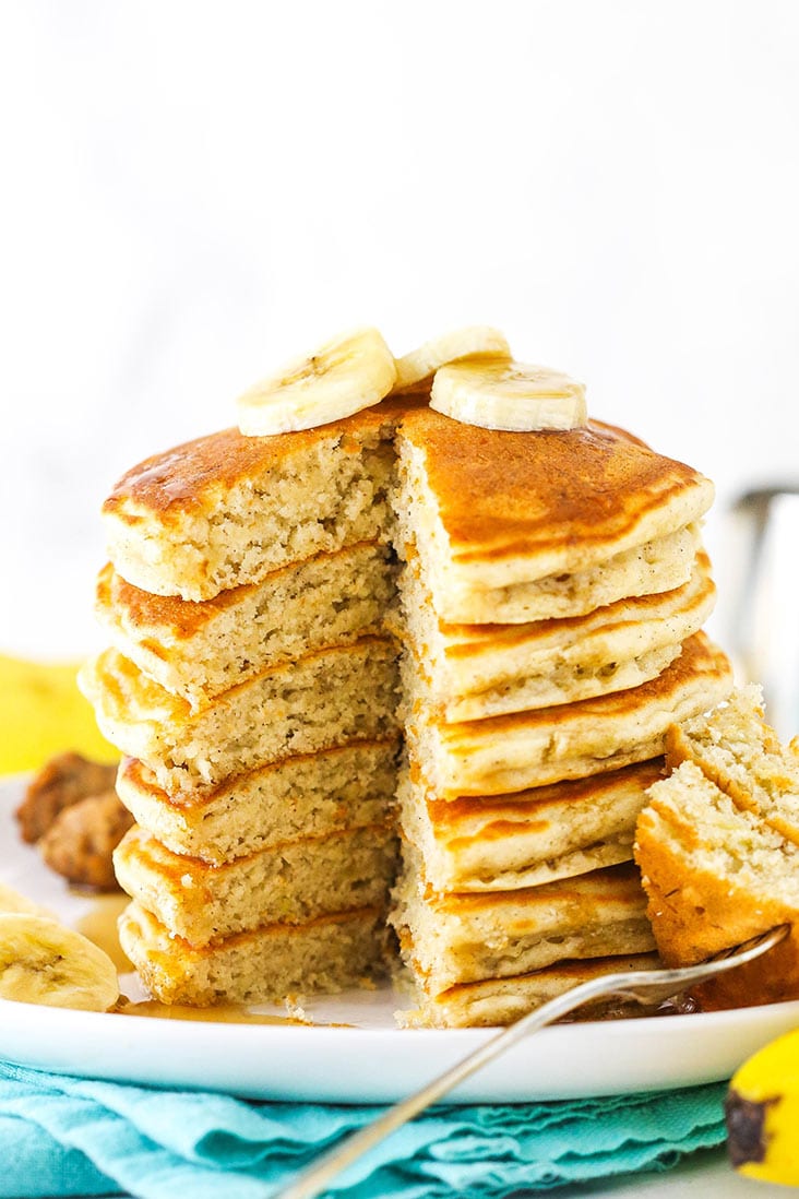 A stack of banana pancakes with one piece missing and slices of bananas on top