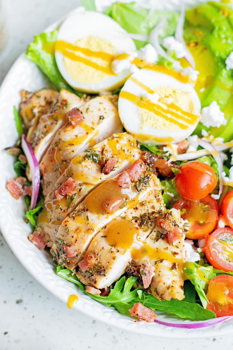 herbed chicken on top of salad with dressing on it