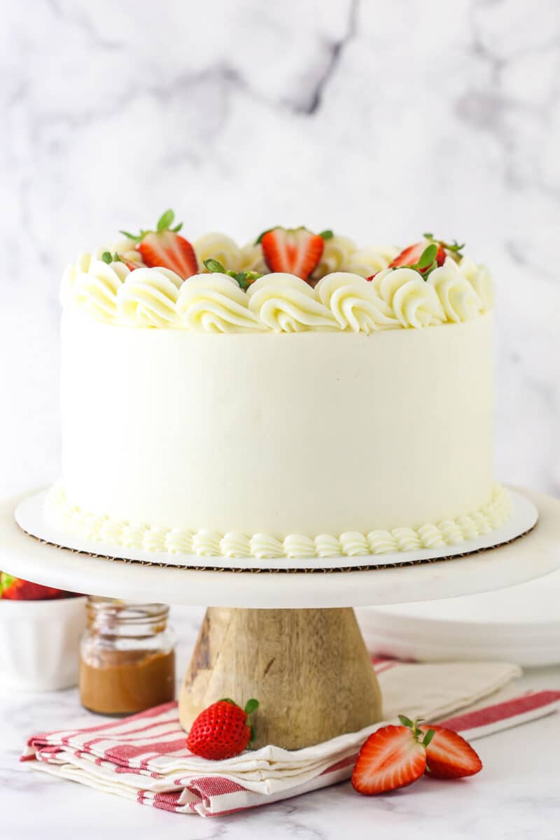 Strawberry Dulce De Leche Cake with white frosting on marble and wood cake stand