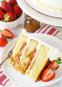 slice of Strawberry Dulce De Leche Cake with strawberries and dulce de leche in background