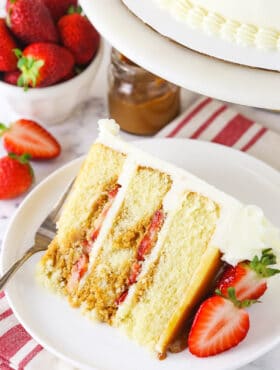 slice of Strawberry Dulce De Leche Cake with strawberries and dulce de leche in background