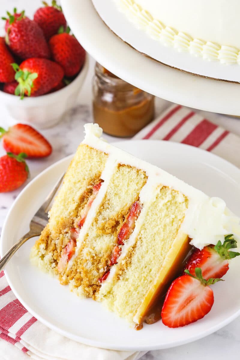 slice of Strawberry Dulce De Leche Cake with strawberries and dulce de leche in background