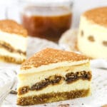 A Piece of Tiramisu Cheesecake on a Plate with a Second Slice and the Full Cake in the Background