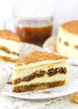 A Piece of Tiramisu Cheesecake on a Plate with a Second Slice and the Full Cake in the Background