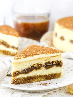 A Piece of Tiramisu Cheesecake on a Plate with a Second Slice and the Full Cake in the Background