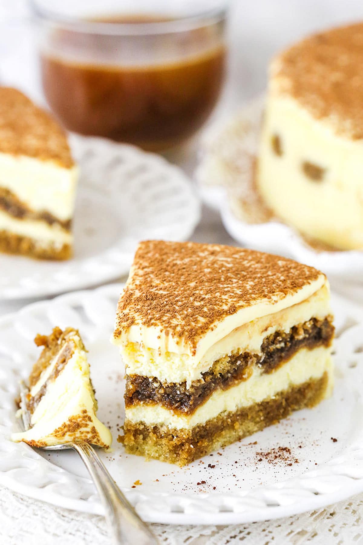 A Slice of Tiramisu Cheesecake on a Plate with One Bite on a Metal Fork