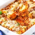 A serving of Italian stuffed shells being scooped from a baking dish