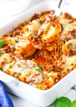 A serving of Italian stuffed shells being scooped from a baking dish