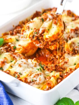 A serving of Italian stuffed shells being scooped from a baking dish