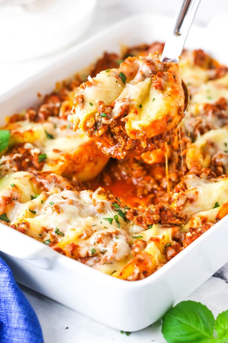 A serving of Italian stuffed shells being scooped from a baking dish