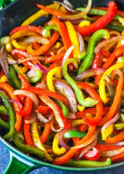 Sliced red yellow and green bell peppers and onions in a skillet