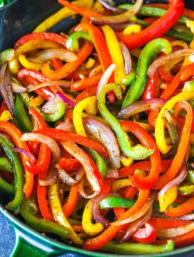 Sliced red yellow and green bell peppers and onions in a skillet