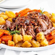Shredded instant pot pork roast on a platter with potatoes and carrots