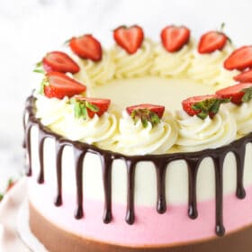 A neapolitan cake decorated with vanilla buttercream swirls, strawberry slices and drips of chocolate ganache