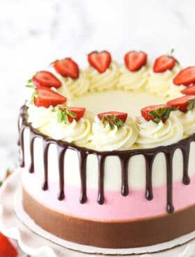 A neapolitan cake decorated with vanilla buttercream swirls, strawberry slices and drips of chocolate ganache