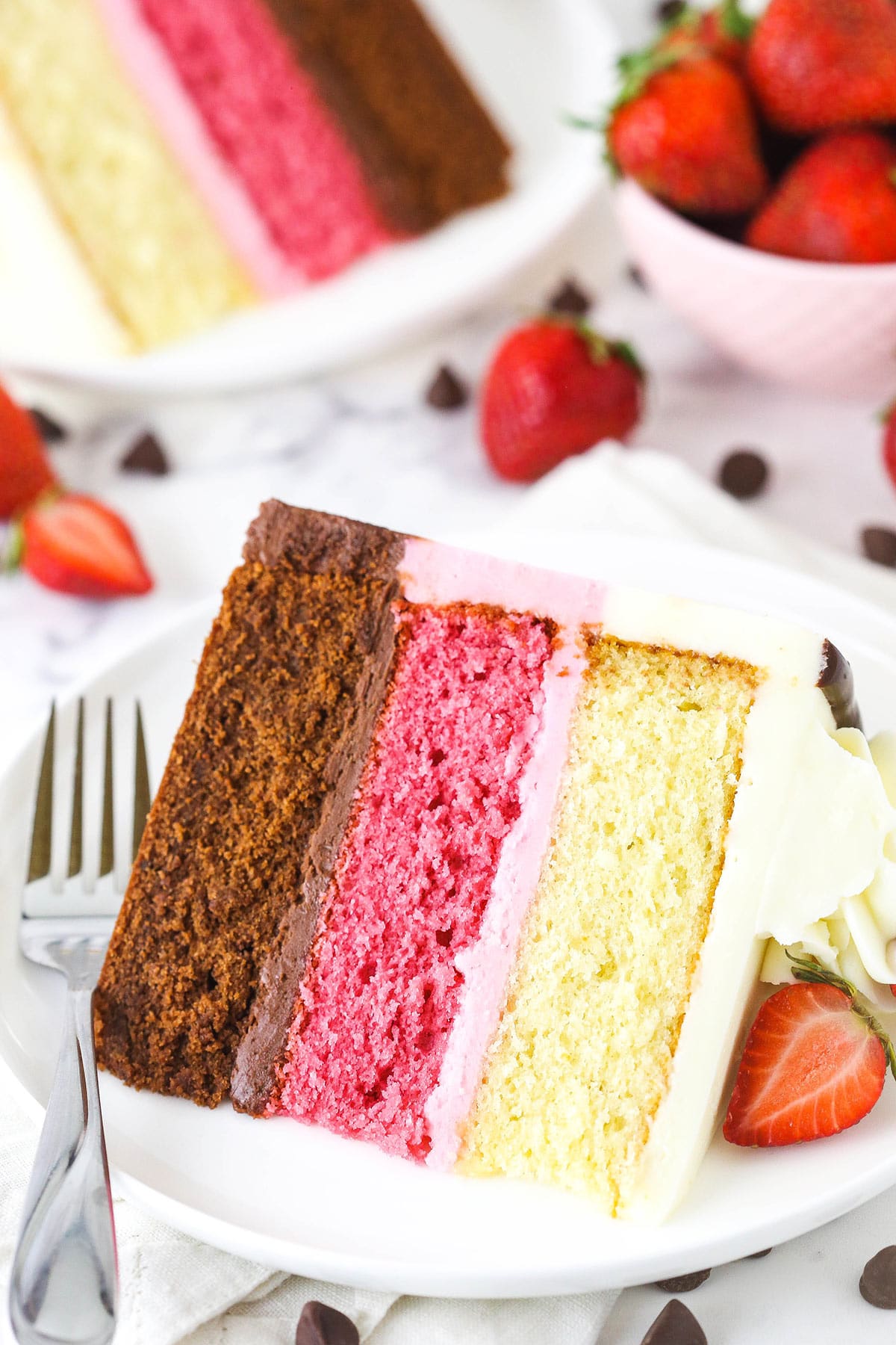 A large slice of neapolitan cake on a plate with a sliced strawberry