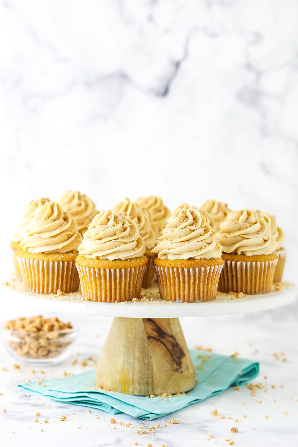 Twelve peanut butter cupcakes arranged on a cake stand with a bowl of peanut butter chips in the background