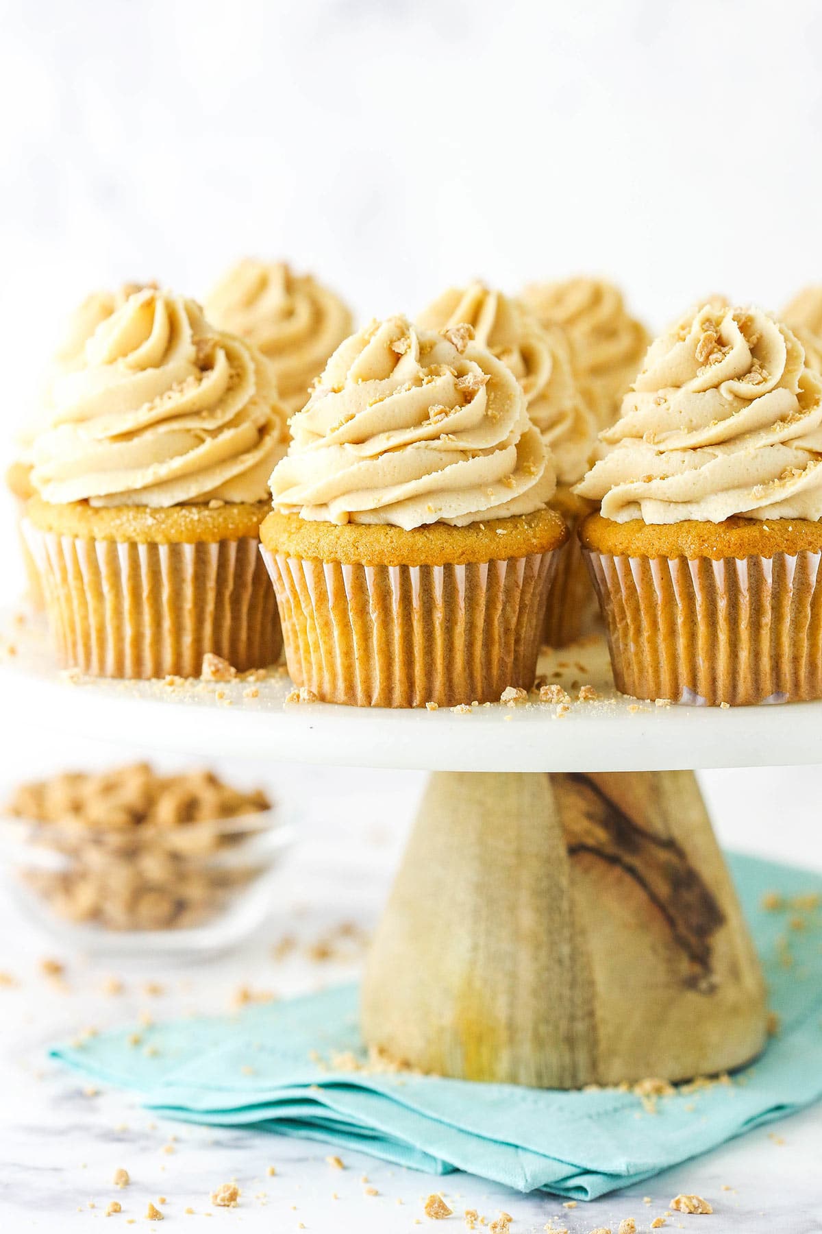 A close-up shot of homemade cupcakes on a white cake stand with a wooden base