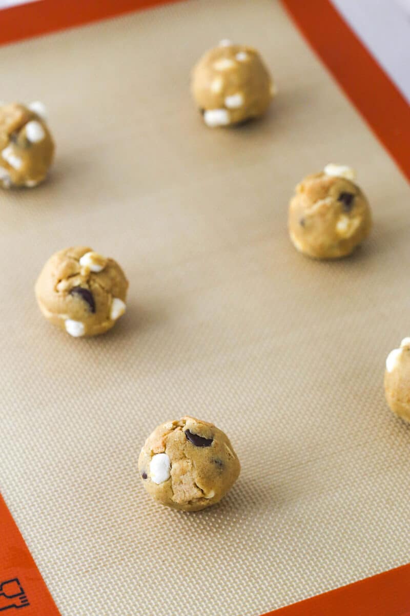 Every bite of these s’mores cookies is loaded with rich chocolate, gooey marshmallows, and sweet graham crackers. Balls of s'mores cookie dough on a baking sheet