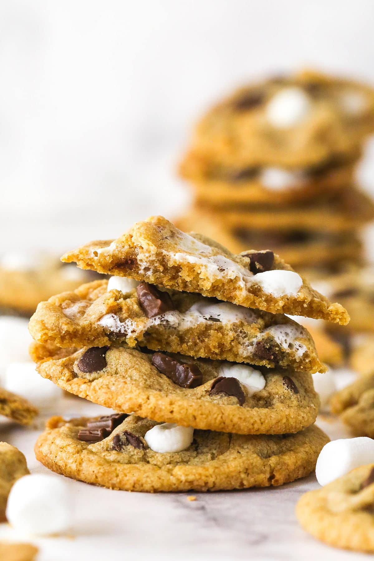 Every bite of these s’mores cookies is loaded with rich chocolate, gooey marshmallows, and sweet graham crackers. A stack of s'mores cookies, one cut in half to show the inside