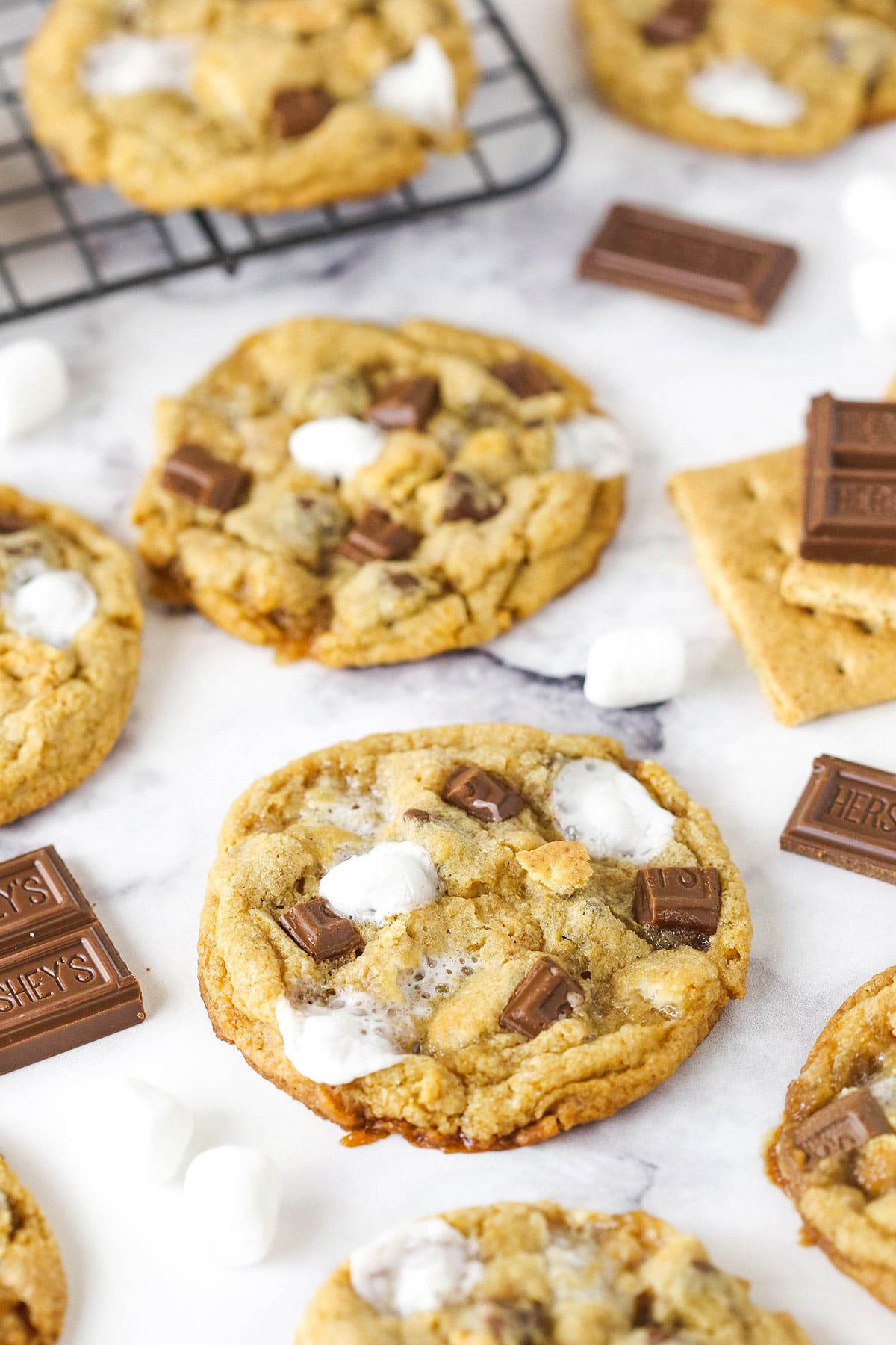 These soft and chewy s’mores cookies are brown sugar cookies filled with chocolate chips, mini marshmallows, and graham crackers! S'mores cookies on a marble table.
