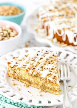 A piece of toffee almond coffee cake on a plate with the full cake and bowls of almonds and toffee in the background